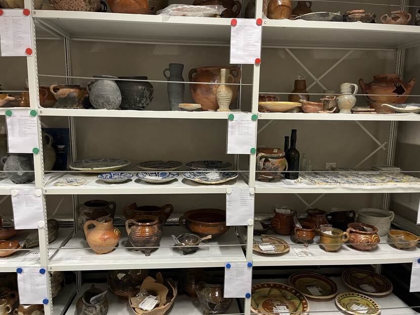 Foto van een depotruimte in het Zeeuws Archeologisch Depot in Middelburg. Op de foto zie je een kast met op de planken allerlei archeologische voorwerpen: zoals schalen en kruiken.