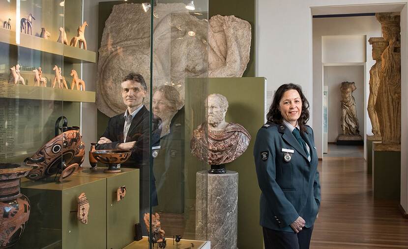 Voorkant van het magazine 'Douane in Zicht' met daarop een douanebeambte en een inspecteur van de Inspectie Overheidsinformatie en Erfgoed in een museale ruimte met archeologische voorwerpen