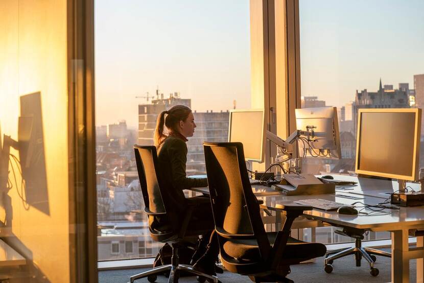 Foto van een vrouw die achter een computer zit in een kantoorgebouw met een gouden ochtendzon