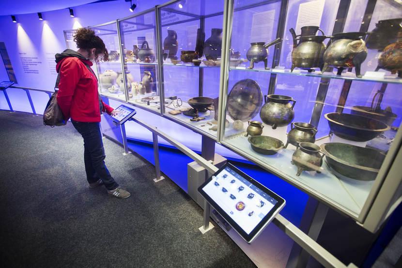 Foto van een Inspecteur in het 'Huis van Hilde' met verschillende tentoongestelde archeologische voorwerpen